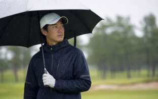 雨のゴルフ場でレインウェアを着たゴルファー