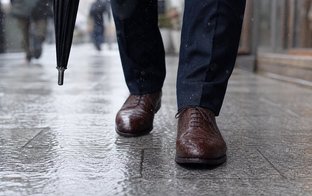 雨の日の日本の街で濡れた石畳を歩くビジネス用の革靴