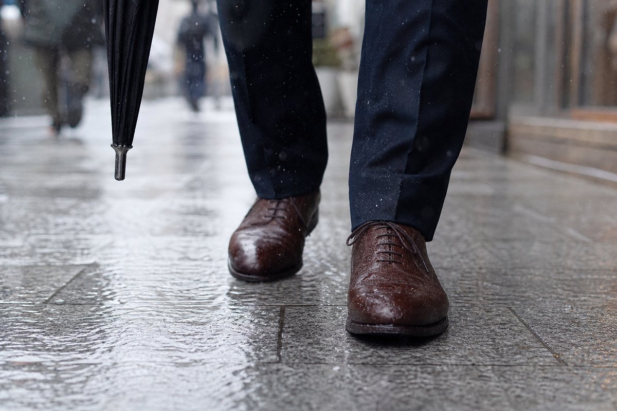 雨の日の日本の街で濡れた石畳を歩くビジネス用の革靴