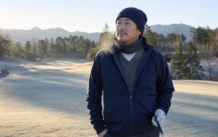 冬のゴルフ場で薄手の重ね着ウェアを着てスイングの準備をする40代の日本人男性